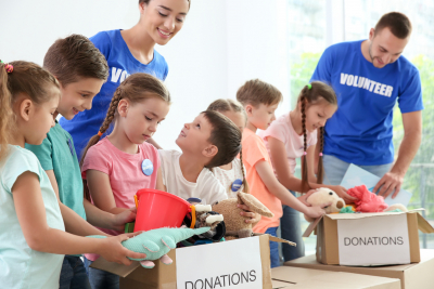 Happy volunteers with children sorting donation goods indoors